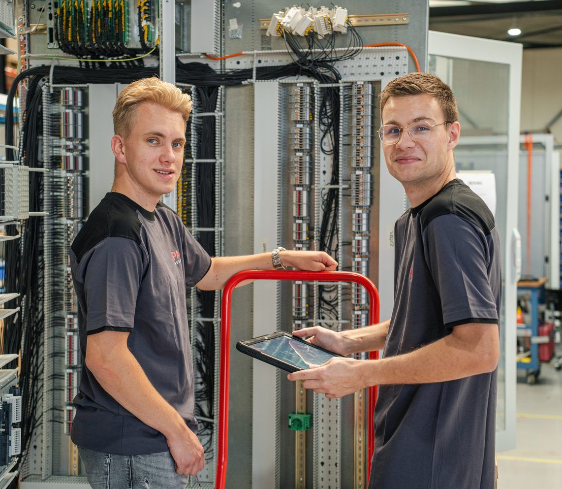 Twee SPARQ-monteurs met een tablet bij een volledig bedraad besturingspaneel