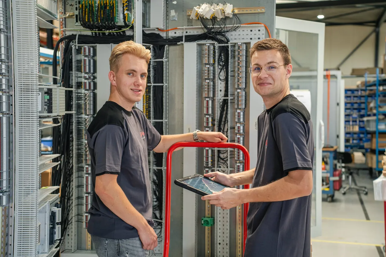 Twee paneelbouwers van SPARQ Assembly bij een bedraad besturingspaneel op de montageafdeling